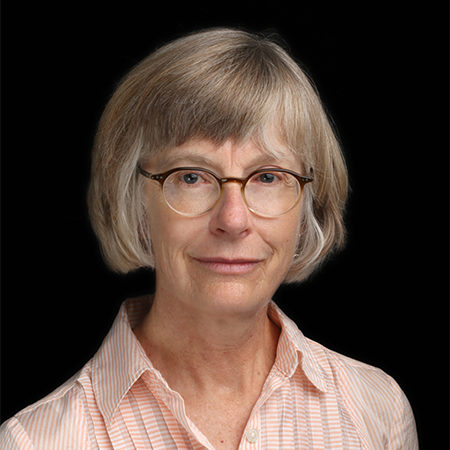 Sheila Dunn, seen from the shoulders up, wearing a pink collared shirt, glasses, and short grey hair